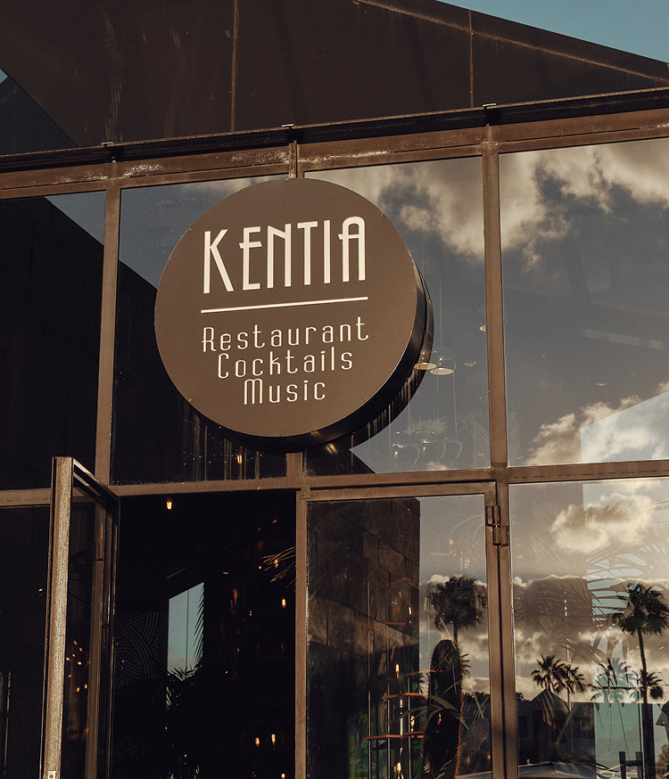 Fachada de cristal y metal del restaurante Kentia en Lanzarote. Cartel circular con el nombre del local y las leyendas 